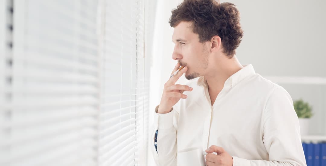 Man smoking near faux wood blinds