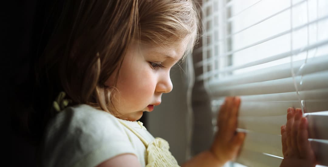 Toddler with hands on venetian blinds 