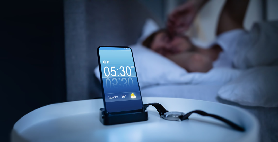 Man in waking up in dark bedroom next to mobile phone 