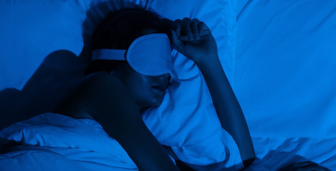Woman asleep in pitch black room with eye mask on