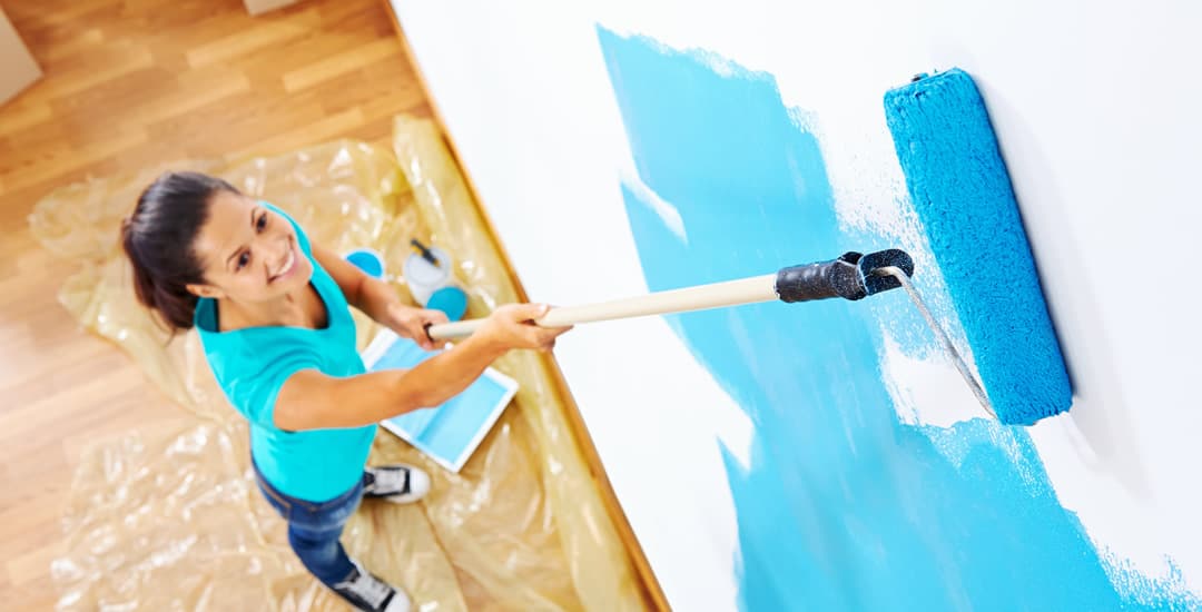 Woman painting wall blue with flooring covered