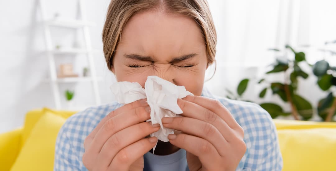 Woman sneezing into tissue due to allergy at home