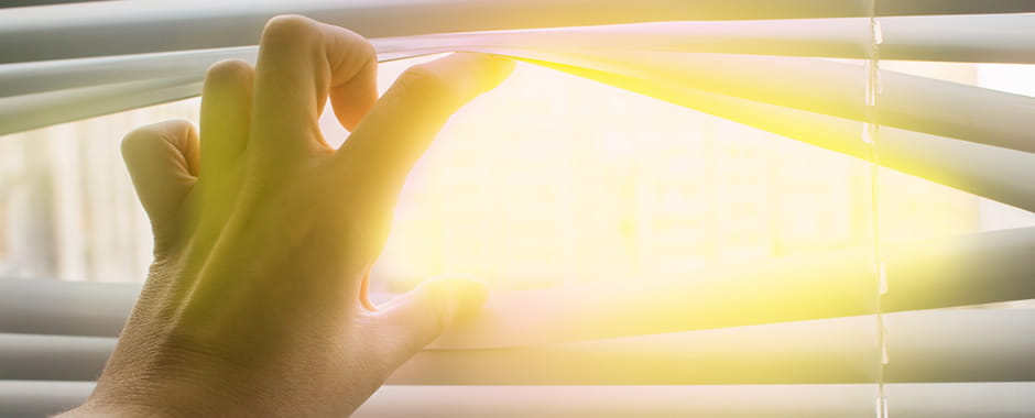 Hand opening venetian blinds to reveal the sun