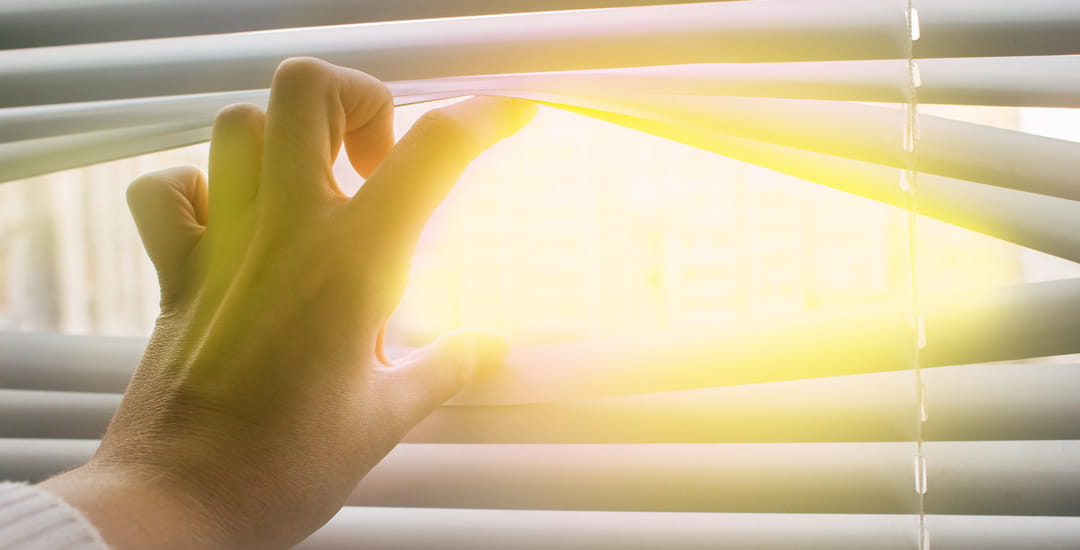 Hand opening venetian blinds to reveal the sun