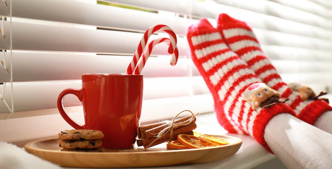 Christmas cookies, drink and socks in front of white wooden blinds