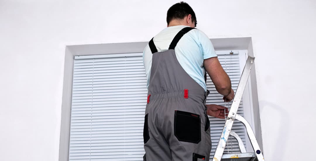 Man, up ladders installing wooden blinds