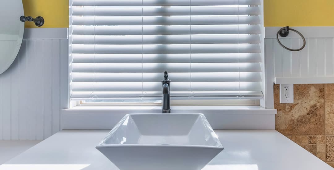 Partially closed white faux wood blinds at bathroom window