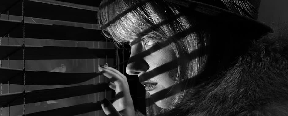 Woman looking through window blinds at night