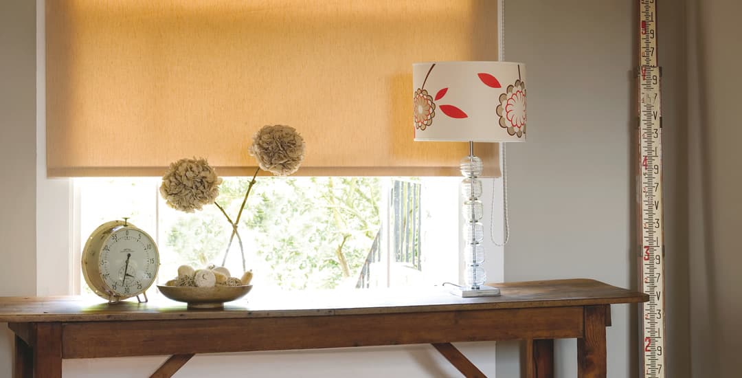 Orange textured room darkening roller blinds in a window above table