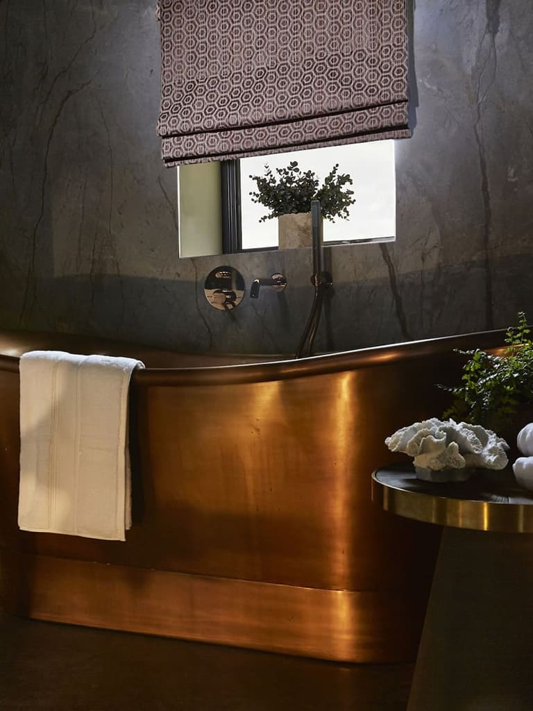 Luxury patterned Roman blind above a burnished gold bath