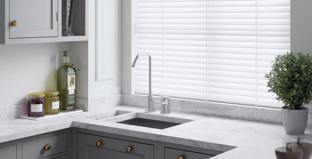 White faux wood blinds made by English Blinds in a white and grey kitchen