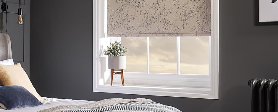 Beige floral patterned roller blind fitted inside recess in a dark grey bedroom