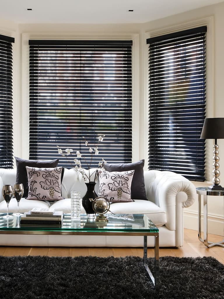 Black wooden blinds in the bay window of a stylish cream living room