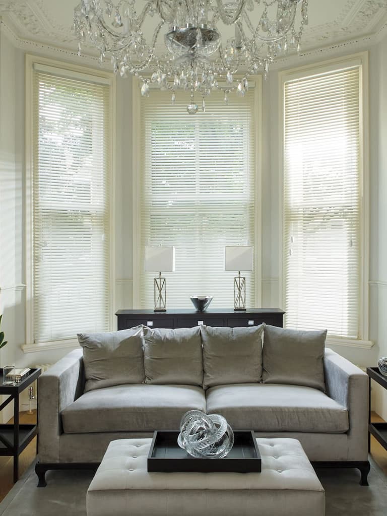 Cream wooden Venetian blinds in a plush high-ceilinged living room