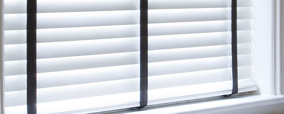 Closeup of closed white wooden blinds with black tapes