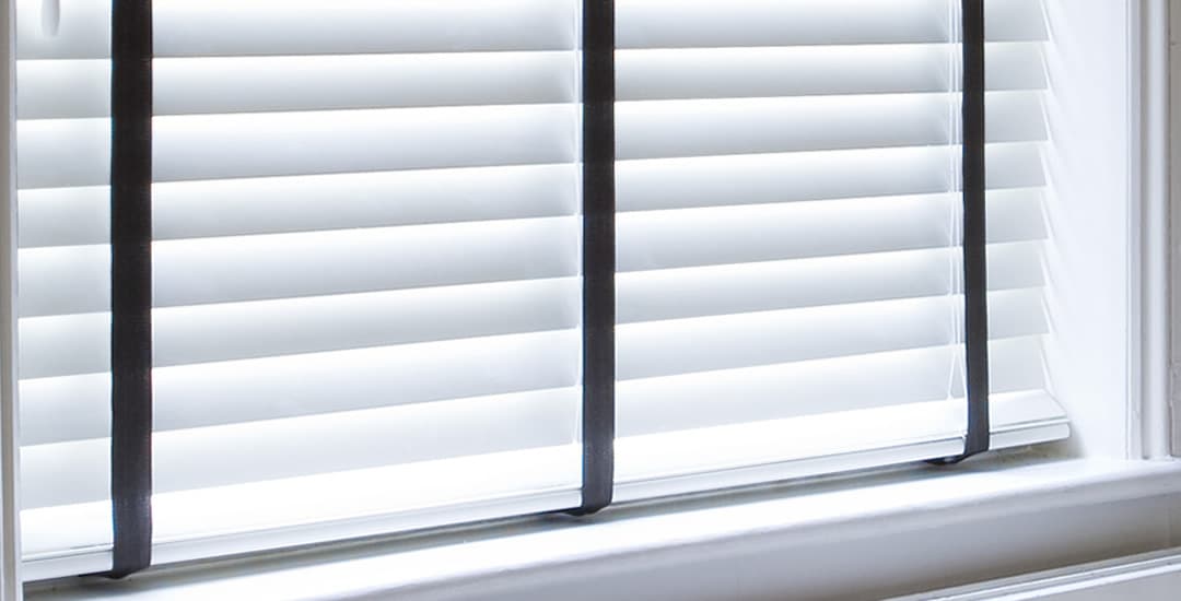 Closeup of closed white wooden blinds with black tapes