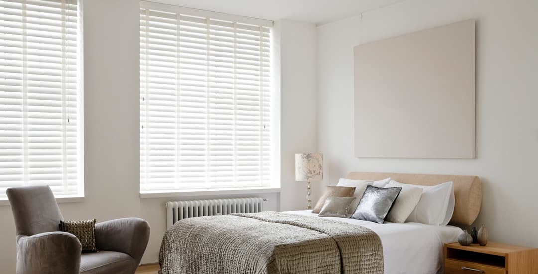 White wooden blinds with tapes in a neutral bedroom