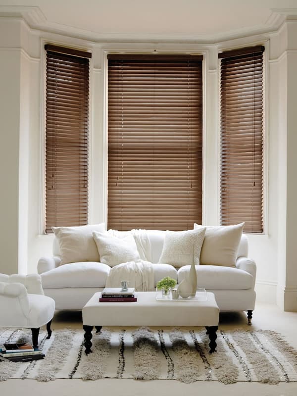 Walnut slatted wooden blinds in the bay window of a cream living room